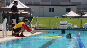 A judge watching over a lifeguard pulling a swimmer from the pool at the Pool Lifeguard Challenge