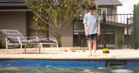 A little boy standing by the pool looking down at the water