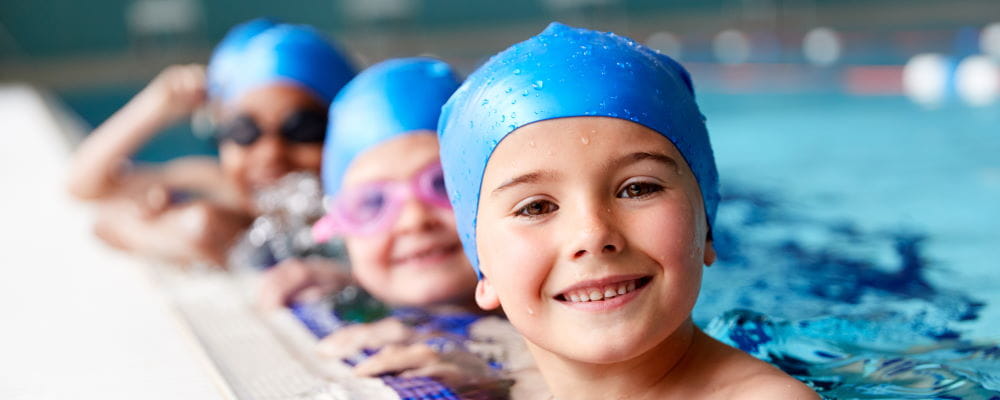 Children along the edge of the pool wearing swimming caps