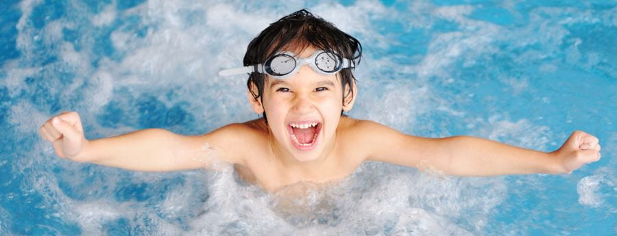 A boy jumping out of the water with arms spread wide and looking very happy
