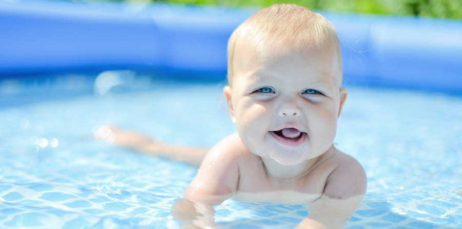 A baby laying on its tummy in a portable swimming pool, smiling