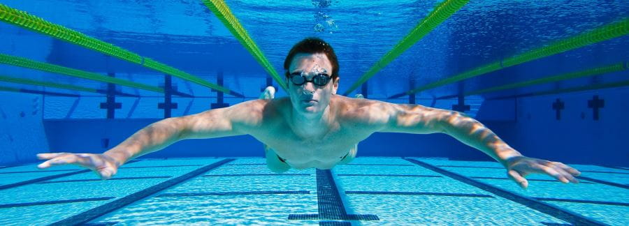 A man underwater in a pool, wearing goggles and with arms spread wide