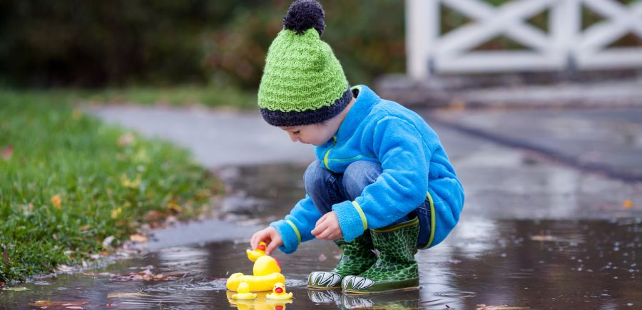 A child rugged up in winter clothes playing with rubber ducks in a puddle