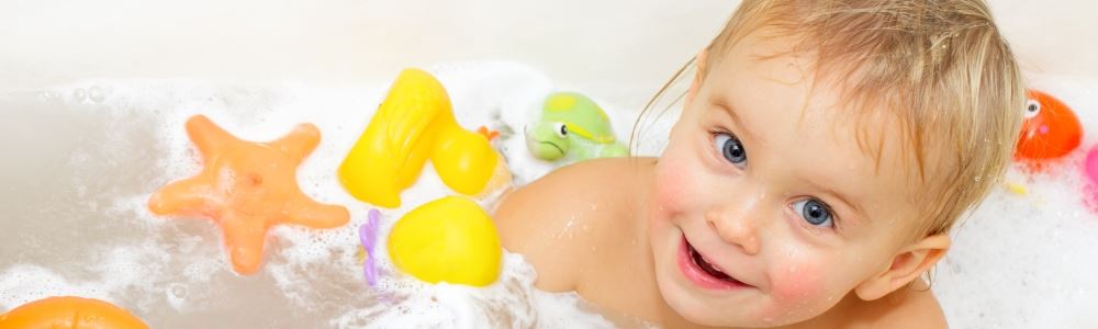 Image of baby in bath with colourful toys, smiling at the camera