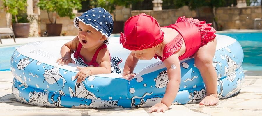 Two toddlers playing in and around a paddle pool, with one almost falling over