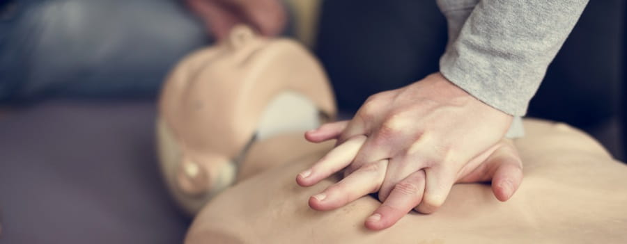 close of person performing chest compressions on a manikin