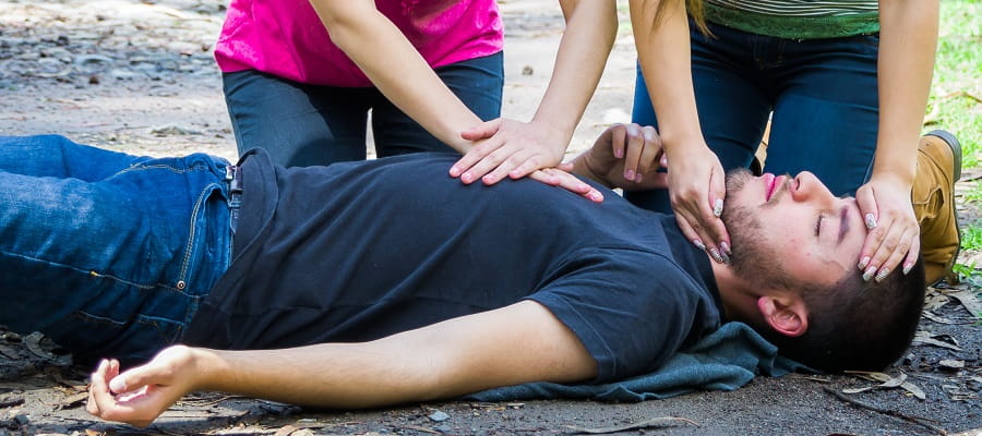 close up of two women performing CPR on unconscious young man
