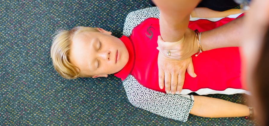 A boy laying on the ground with a person performing CPR on his chest
