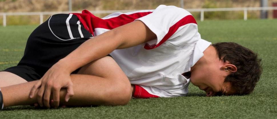 A teenage boy laying on the grass gripping his leg with face on the ground