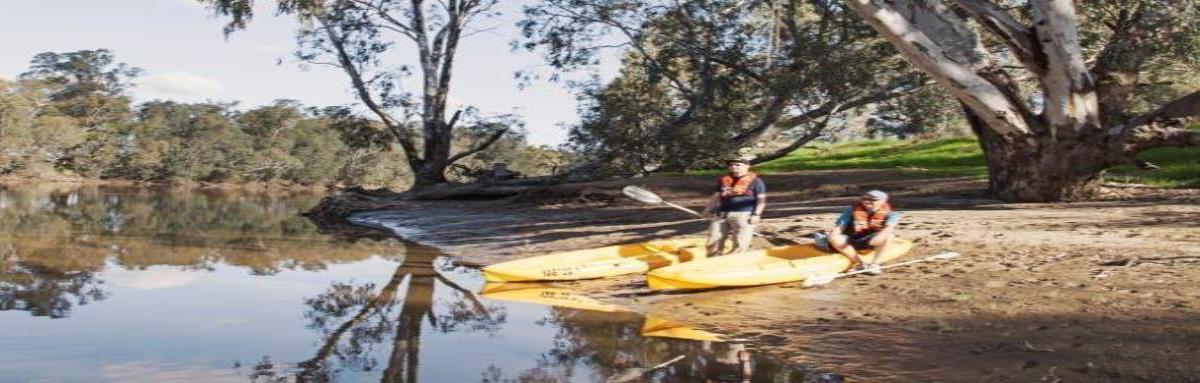 Two people with their kayaks standing beside a river