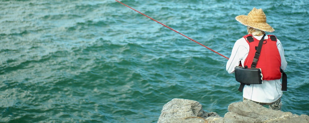 man wearing lifejacket fishing from rocks