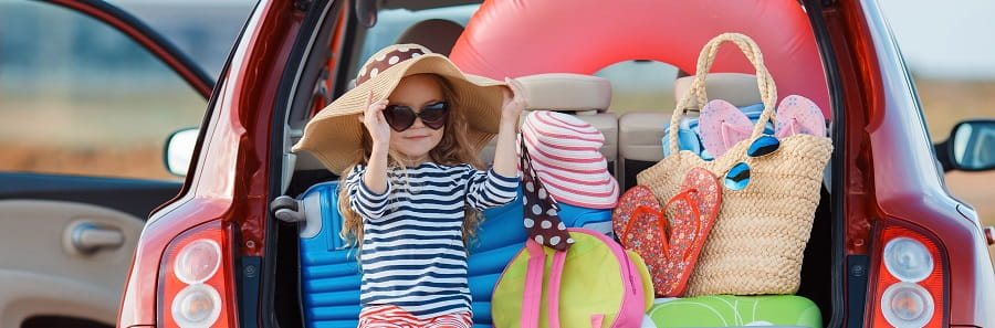 little girl wearing hat and sunglasses sitting in the open boot of a hatchback