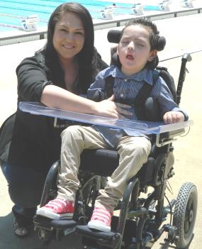 Simone Soto-Flores crouching beside her son Ari in his wheelchair